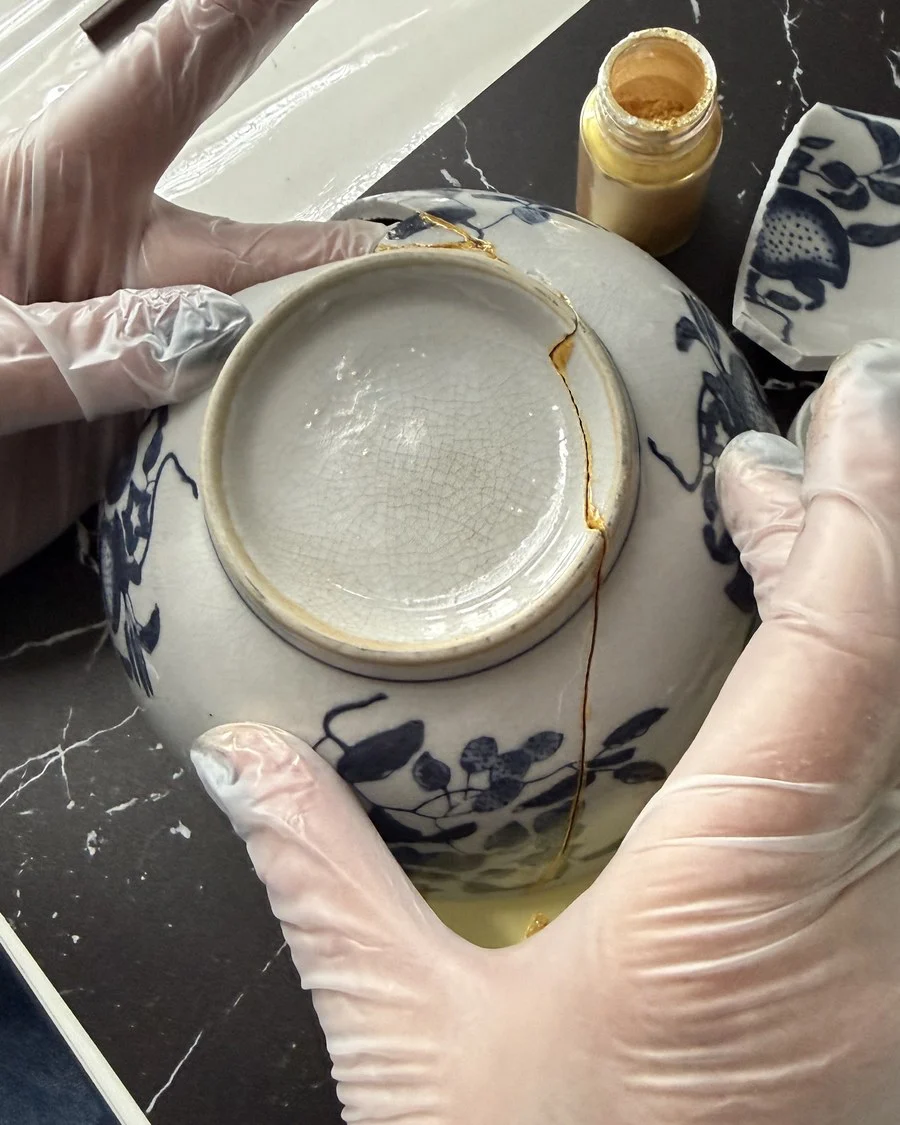 Close-up van handen die met goud een kintsugi-herstel aanbrengen op een kopje